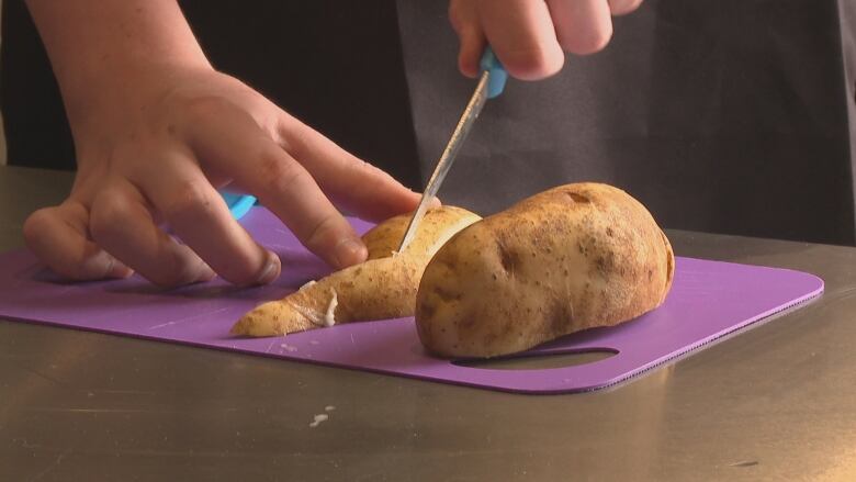 A close up of a kid slicing a potato into french fries.