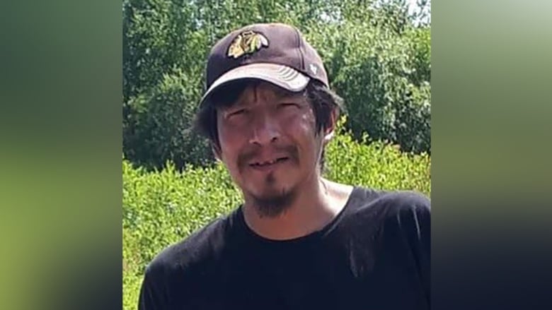 Man in a black t-shirt and hat looks at the camera