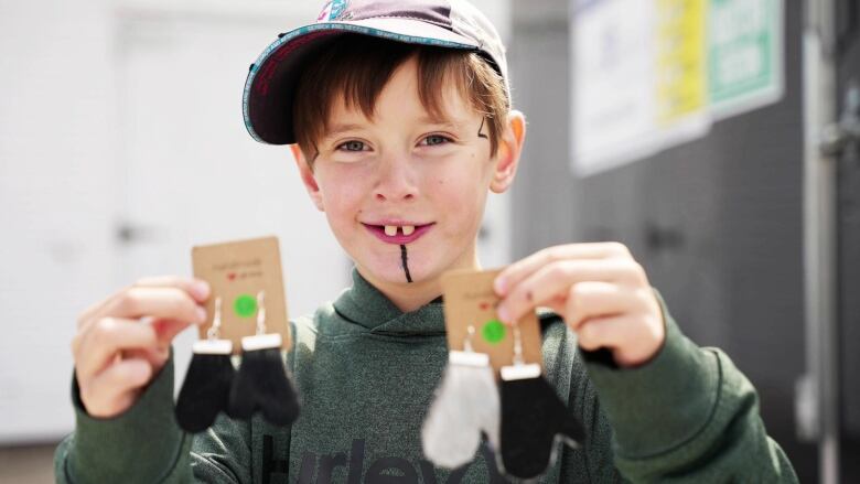 A young boy with traditional Inuit tattoos holds up earrings showing sealskin mittens. 