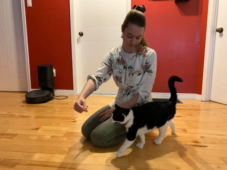 A young woman sits on the floor and plays with her black and white cat