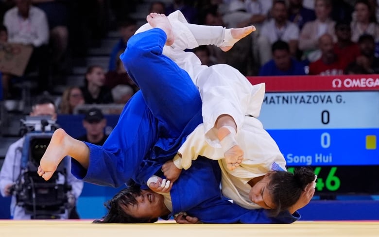 Two women, seemingly falling over each other, compete in martial arts. 