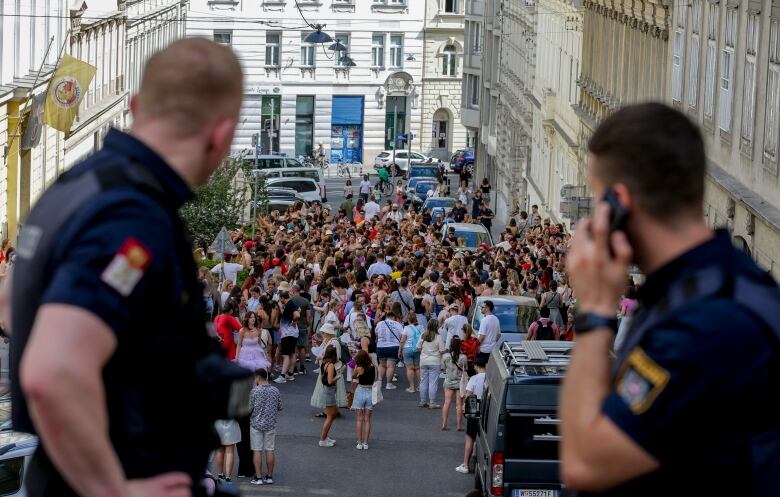 Two police officers watch a crowd of people on a street.