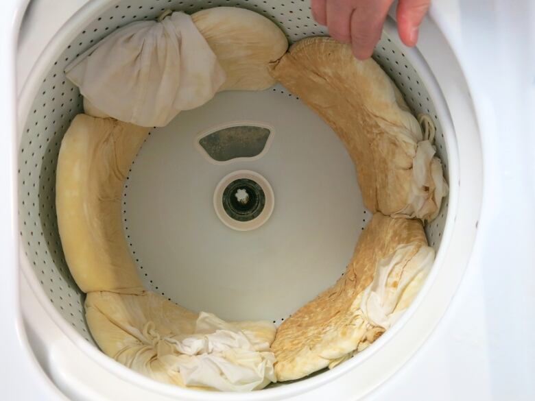 A washing machine is shown with several cheese cloth bags inside of it. The bags have grated potatoes in them.