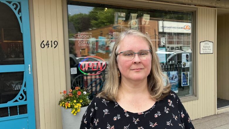 A woman wearing glasses standing in front of a building looking solemn. 