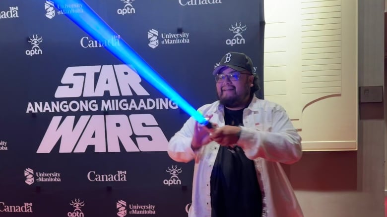 A man hold a blue-coloured light sabre in front of a Star Wars poster