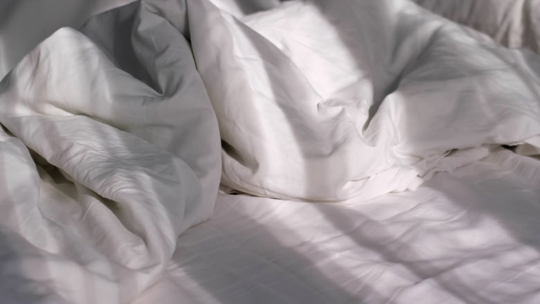 closeup on an empty, unmade bed with white linens. sun shines on the bed creating shadows. 