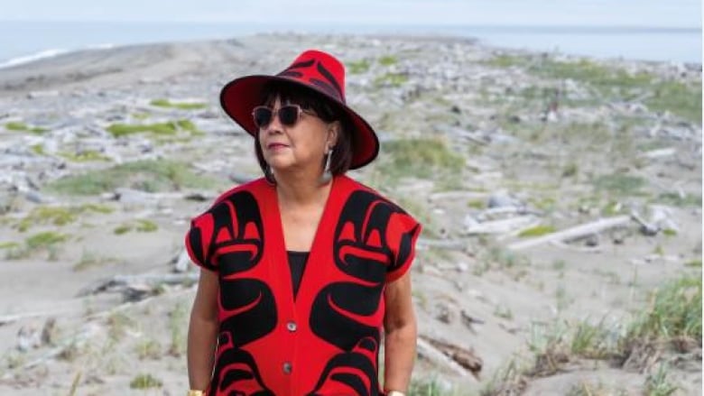 A woman standing in tall, green grass while wearing a black and red hat and dress. 