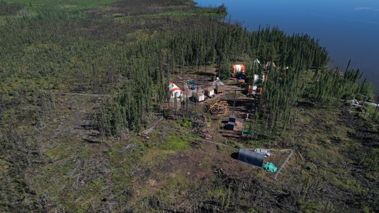 An aerial photo of a camp site in forest. There are a few orange and white structures. 