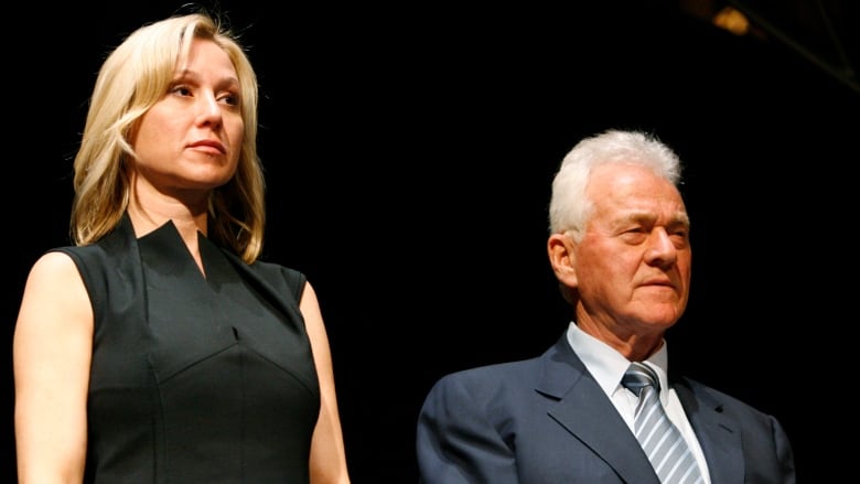 A woman with blonde hair stands next to an older man with grey hair