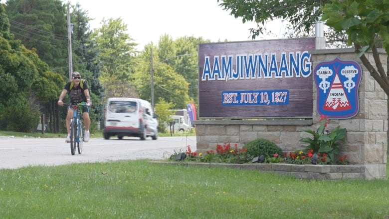 a man on a bicycle rids past a sign for the community of Aamjiwnaang First Nation