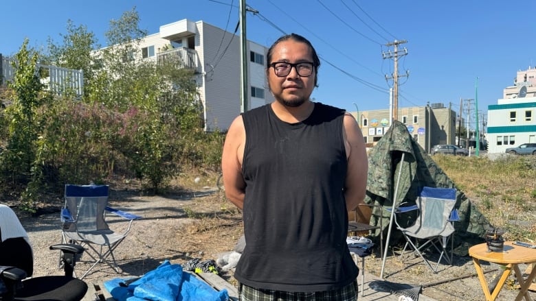 Man in flannel shorts stands in front of tent