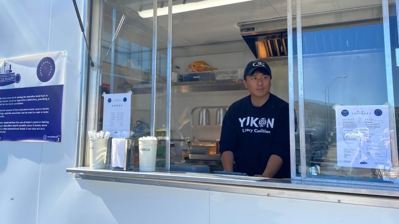 A man stands at the window inside a food truck.