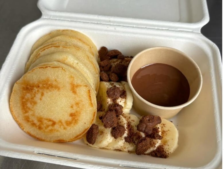 A styrofoam tray of pancakes and chocolate sauce.