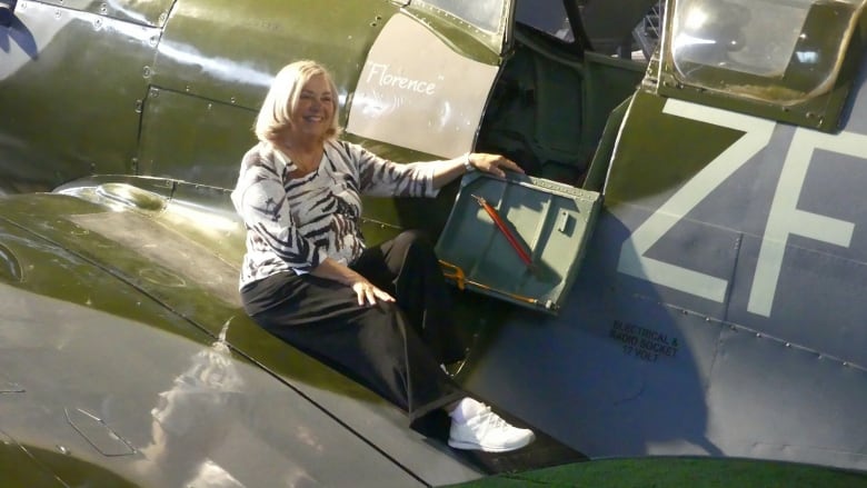 A smiling woman with blond hair sits on the wing of a Spitfire plane at a museum in Krakow, Poland.