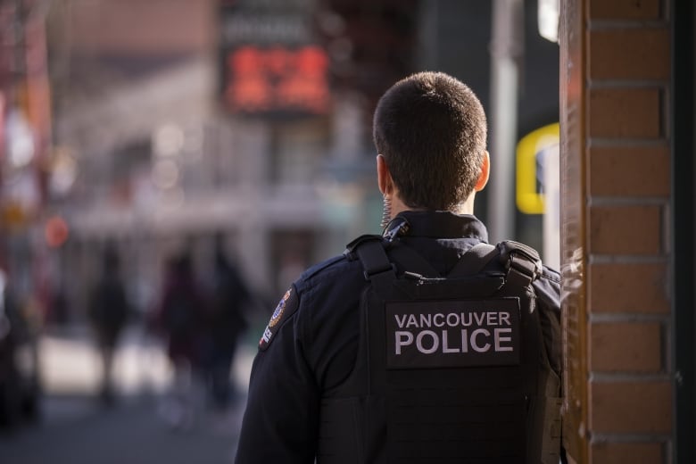 A person with 'Vancouver Police' on their back leans against a wall.