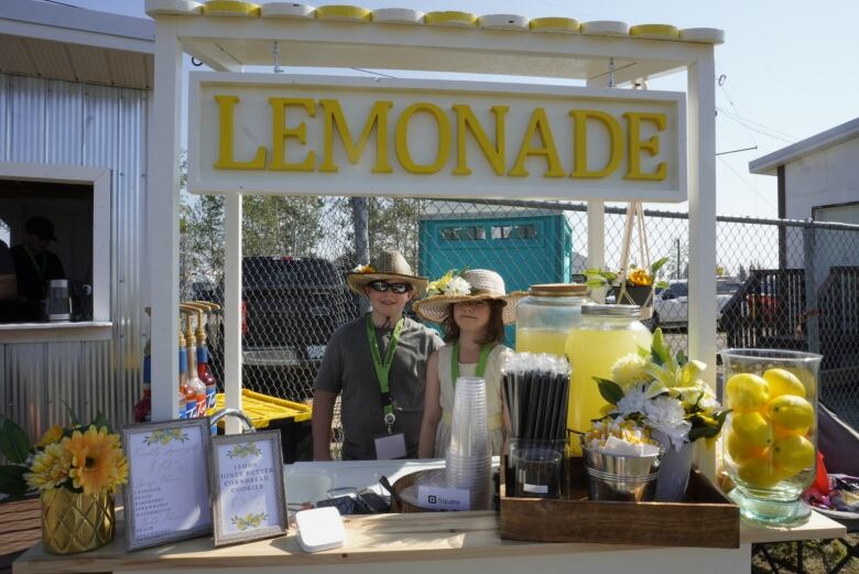 Two kids in big straw hats stand behind professional looking lemonade stand