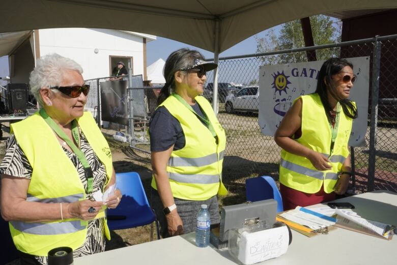 Three women in safety vests give out tickets at a booth