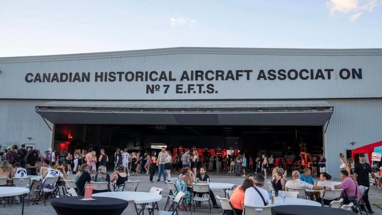 People gather inside and outside a dance music party at an aircraft hangar.