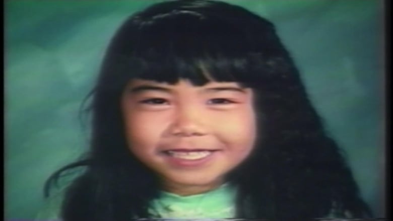 An East Asian girl smiles while against a green background.