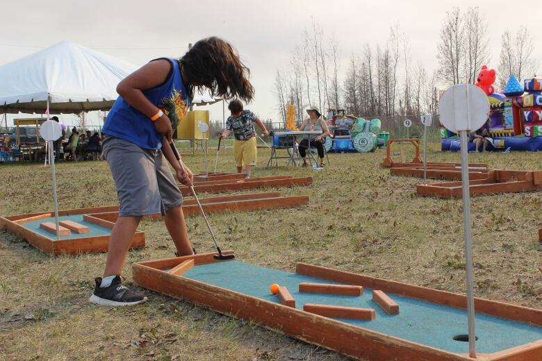 A kid plays mini golf. 