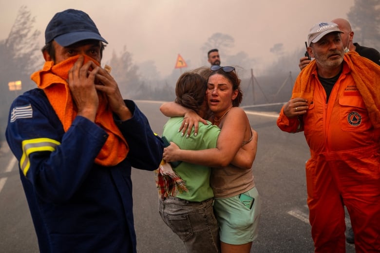 Two women hug with rescue workers on either side.