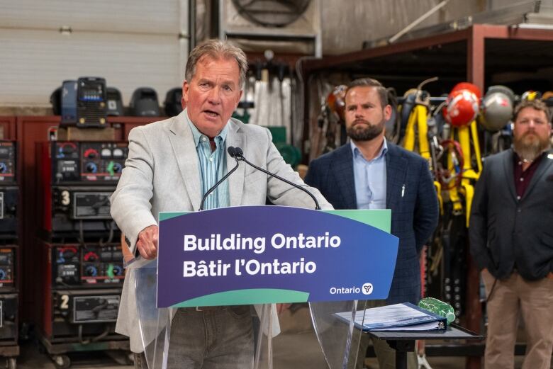 A person wearing a suit is seen standing at a podium and speaking into a microphone.