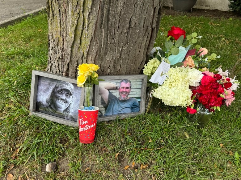 A memorial for 67-year-old Walter Lasher of Greater Napanee, photos, flowers and tim hortons cups surround a tree. 