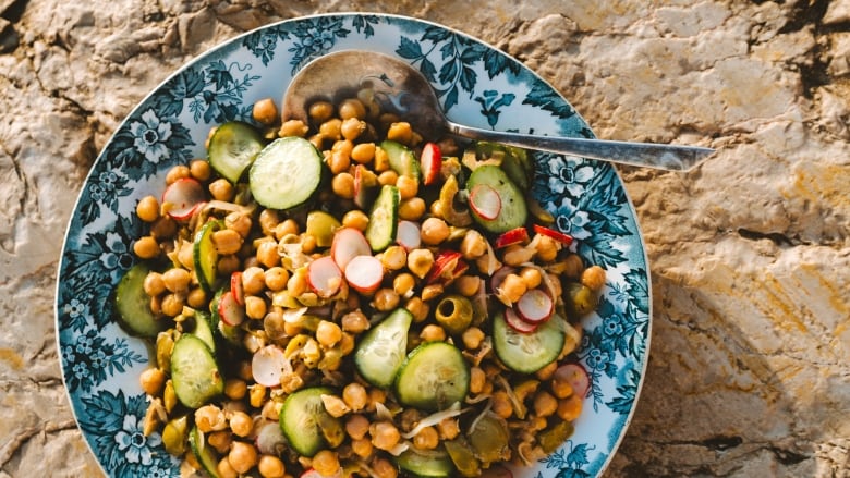 Closeup on a blue patterned plate of chickpea salad sitting on a large rock. 