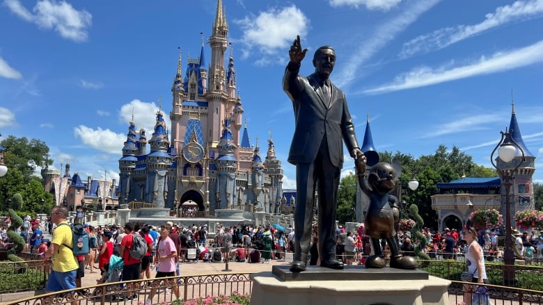 People walk behind a statue, with a castle in the background.