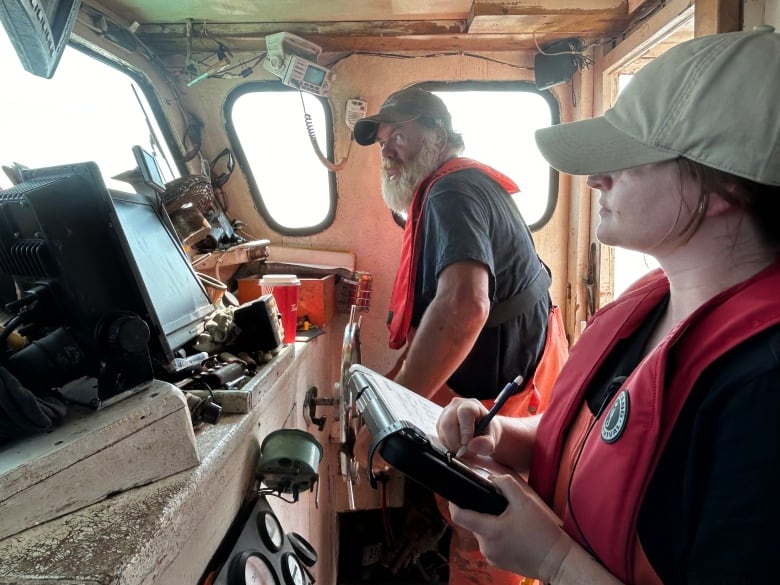 A woman writing in a notepad as a fisherman steers his boat.