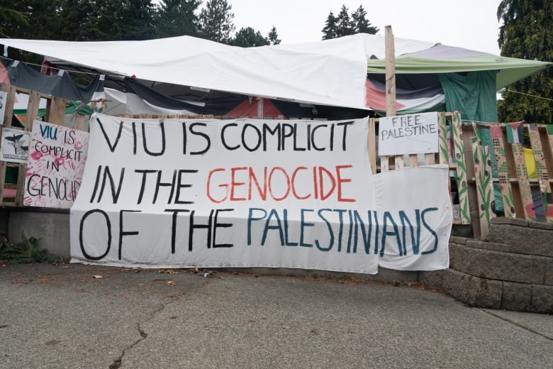 A pro-Palestinian encampment with a provocative all-caps banner accusing the institution of complicity.