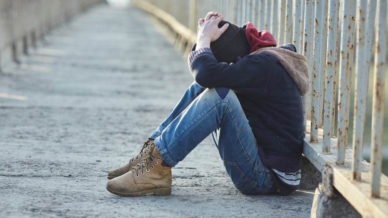 a person is seen sitting on the ground on a concrete bridge with their face buried in their hands.