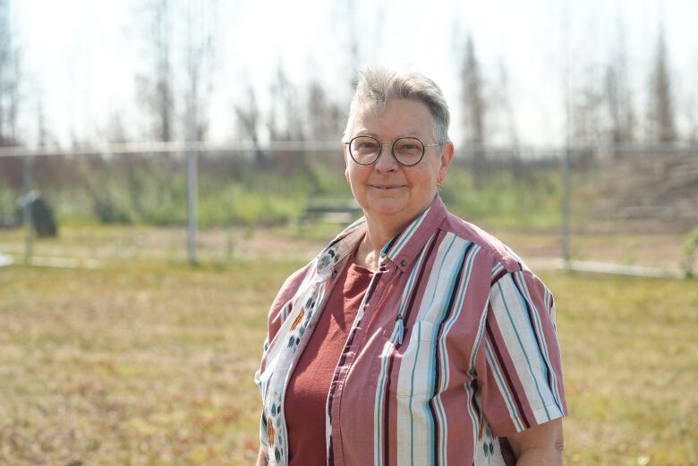 Woman in glasses and striped button up stands in field.