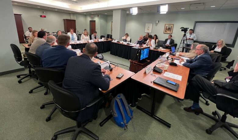 A group of people in a room seated around tables facing each other.