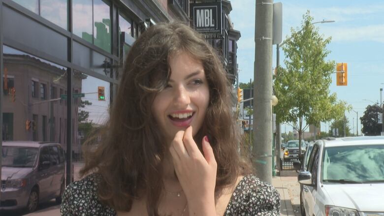 A young woman on a sidewalk answering questions.