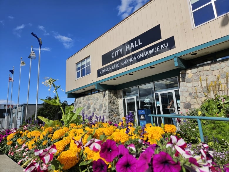 Colourful flowers in the foreground, flags of First Nations, Yukon, Canada, entrance to Whitehorse city hall