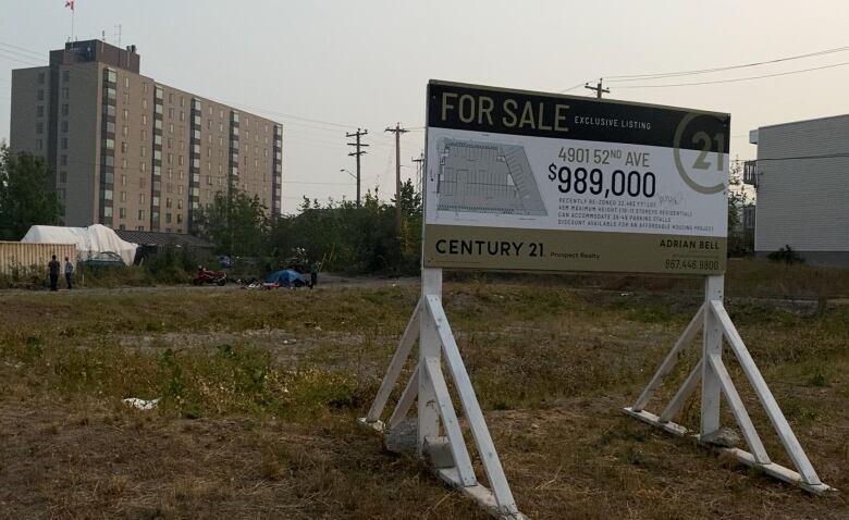 A big sign listing a vacant lot for close to $1 million. Tents in the background.