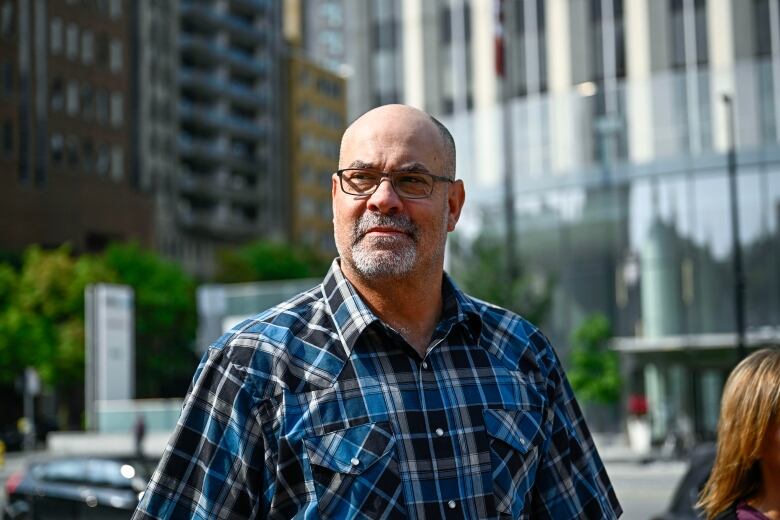 A bearded bald man in a blue plaid shirt and glasses.