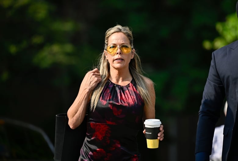 A woman in a black and red top and yellow sunglasses holds a cup of coffee.