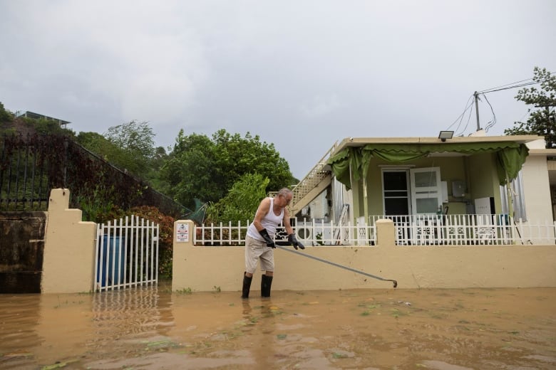 A man stands in deep water holding a  rake in front of a  house