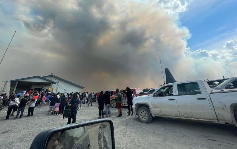 People stand at an airport with smoke billowing in the air