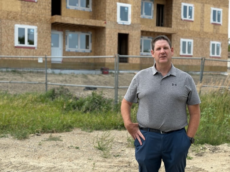 Man in gray shirt stands in front of fence and apartment building under construction