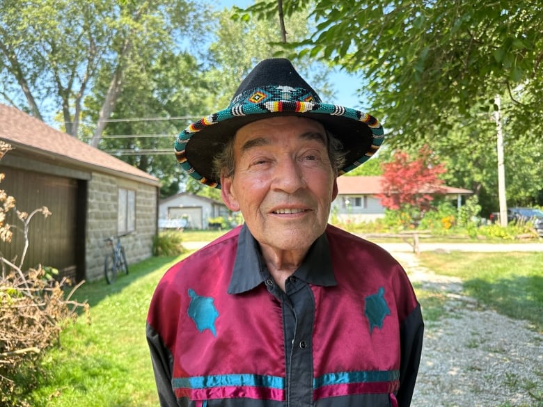 A man stands in a yard, wearing a hat.