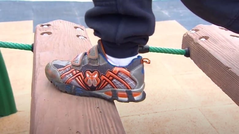 Leg and sneaker of school age kid playing on playground structure. Walking across wooden plank bridge.