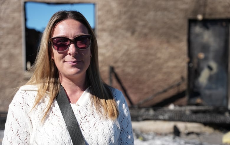 A woman stands in front of a burned building. 