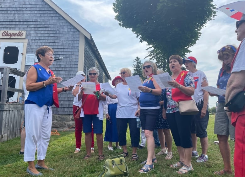 a group of women sing outside dressed in Acadian colors