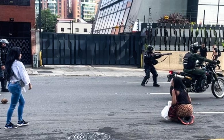 A woman kneels in the street as military point guns during a protest in Caracas following the country's disputed July 28 election.