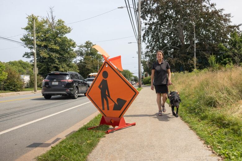 Woman and dog walking past a sign of 