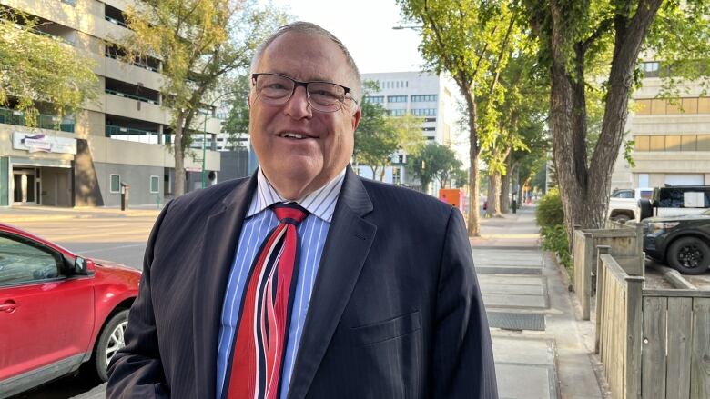 A man in a suit stands on the sidewalk during the day.