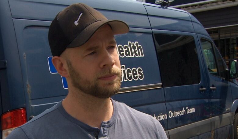 Man in baseball cap stands in front of large van.